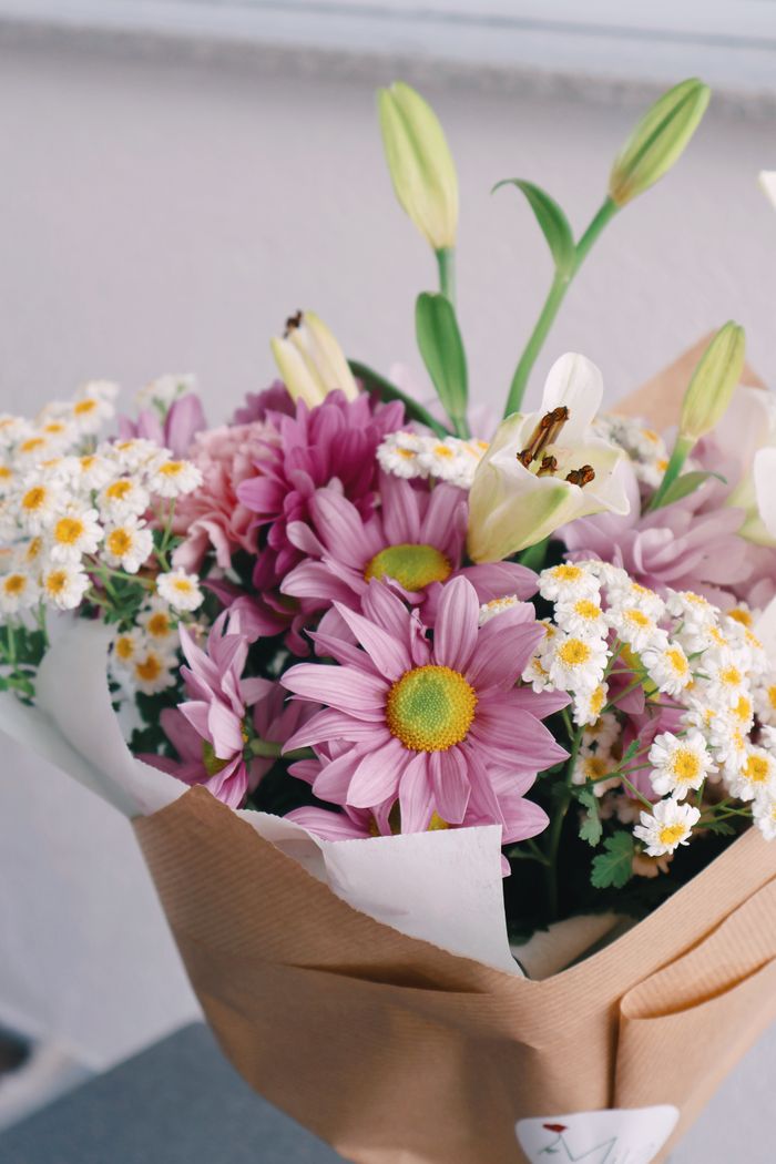 Beautiful spring bouquet featuring purple daisies, white lilies, and chamomile flowers arranged elegantly.